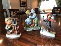 Full view of the three figurines on a wooden table, showing the boy with camera, the couple figurine, and the skiing boy.