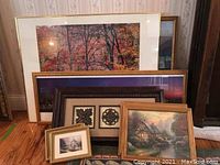 Photo of 7 framed wall art pieces, varying sizes with autumn trees, purple mat landscape, and cottage scenes