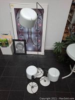 Three lamps displayed together on tiled floor with artwork in background