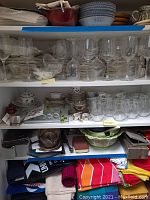 Top shelf showing assorted clear glass wine glasses in front of wrapped porcelain plates