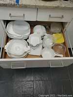 Drawer filled with white CorningWare and glass bakeware and dishes including lids, with blue cornflower pattern visible on dish bottom.