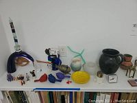 Wide view of various decor items and pottery on a white shelf, including candle holders, small animal figurines, and a large black pot.