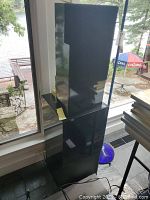 Two black speaker modules stacked (top and bottom) in front of window overlooking lake