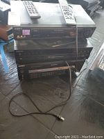 Stacked Sony electronics including a video cassette recorder, compact disc player, and digital audio/video control center with two remote controls on top.