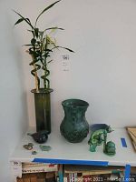 Bamboo plant in tall green glass vase with ceramic and glass decor on shelf
