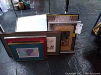 Multiple framed wall art prints resting against a glass window, showing various sizes and frame colors.