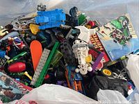 Closeup of assorted Lego pieces and sets mixed in a plastic bag showing various parts and colors.