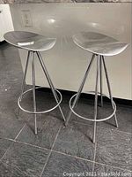 Front view of both stools showing molded seats and tubular legs on black tiled floor