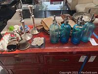 Full lot view showing all items arranged on a wooden table, highlighting bells, candlestick holders, drink decanters, cutting boards, and baskets.