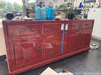 Front view of red wooden Asian-style buffet with floral painting and metal hardware, showing four top drawers and four lower cabinet doors.