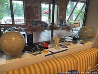 Wide view of window ledge displaying two monochrome globes, one colored globe at right, measuring instruments and storage boxes.