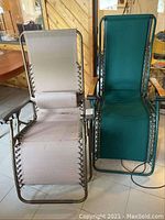Two zero gravity lounge chairs shown side by side, tan stained chair on left and green chair on right, both with metal frames and wooden armrests.