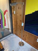 Full view of the floor lamp showing entire height and base, positioned next to a wooden paneled wall and doorway.