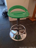 View of green plastic seat swivel stool from the side showing seat and chrome base with footrest ring.