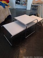 Three nested white top tables on chrome tubular frames in a room with slate floor.