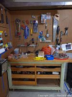 Workbench with assorted hand tools, cords, and hardware on top and pegboard with hanging tools