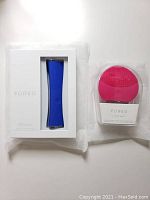 Two FOREO skin care devices in original boxes shown side by side on white background. Left is the blue Espada acne treatment device in white box, right is the pink Luna Mini 2 in clear plastic casing.