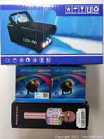 Boxed professional LED-500 fog machine with changing lights, two boxed LED party lights, and boxed rose gold wireless microphone with LED lights.