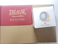 Photo showing the Reacher R2 white noise machine packaging on top of the Caterbee mobile box with red and beige color.