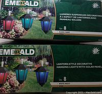 Two unopened boxes of Emerald brand lantern-style decorative hanging lights with solar panels, one showing 3 colored lanterns in red, turquoise, and blue with black top.