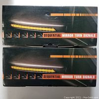 Two unopened black boxes of sequential mirror turn signals, displaying product name and product image of amber LED strip on side mirror.