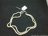 Full view of off-white round pearls arranged on black background with tag