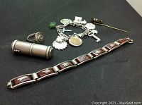 Overview photo of all sterling silver items including charm bracelet, lipstick holder, ring, link bracelet, and amber pin on black background