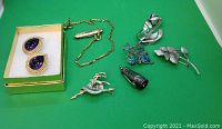 Full lot showing gold and amethyst stone earrings in a box, sterling silver cigar cutter on chain, multiple silver brooches including floral and bird designs.