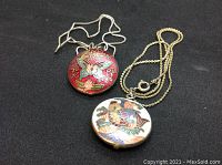 Overview of both cloisonné pendants with their sterling silver chains laid side by side on black background