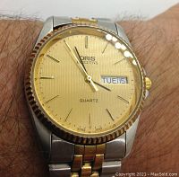 Watch on wrist showing gold-tone dial, fluted bezel, day-date display and two-tone bracelet for scale.