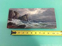 Front view of rectangular wood panel painting depicting crashing waves against cliffs with measuring tape showing width approximately 12 inches