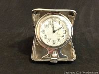Front view of the clock opened in its sterling silver case, showing white dial with Arabic numerals and ornate hands