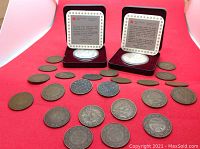 Overview of two presentation-case silver dollars and twenty-two copper one cent coins arranged on red background