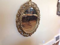 Full view of the oval gilt antique mirror hanging on the wall, showing overall design and condition.