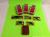 Three American Girl doll boxes, six Marx Collectors Series replica cap guns carded, vintage red Mutual Life book-shaped piggy bank on green background