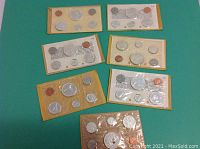 All seven sealed coin sets arranged in two rows on green felt