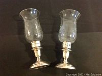 Two Birks sterling silver candlesticks each fitted with a crystal hurricane shade. Both shades have an incised grape design and are slightly different in shape.