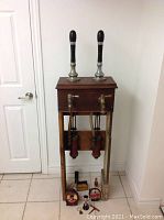 Full frontal view of the entire wooden beer dispensing system with two black-handled taps and items beneath