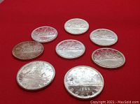 Reverse side of all eight coins arranged on red background, showing canoe design and dates.