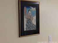 Overview of one framed Japanese woodblock print on wall, gold gilt frame and black mat