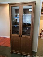 Exterior view of wood curio cabinet with glass panel doors, closed, showing wooden frame and handles.