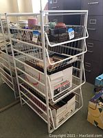 Front and side view of white metal wire storage rack with 4 pull-out drawers, containing boxed office paper and miscellaneous items.