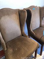 Pair of brown fabric wingback chairs shown side by side from a slight angle.