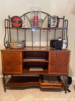 Front view of wooden sidebar with metal trim and shelving, showing decorative carved cabinet doors, open center shelves, and metal frame with hanging rod.