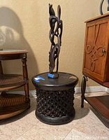 Front angle of the decorative stand with the carved wooden statue placed on top.