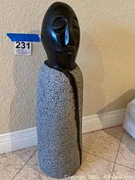 Front view of the solid stone sculpture showing the black carved face with closed eyes and the textured gray stone body.