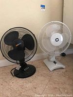 Two oscillating fans: one black with three buttons and one white with three sliders on base.