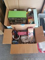 Full view of a cardboard box filled with assorted hardware items including tools, electrical outlets, and accessory kits.