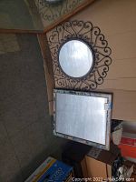 Photo showing both the round wrought iron framed mirror and the rectangular tiled framed mirror together on the floor against a wall.