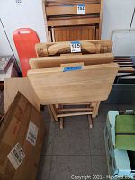 Four wooden folding TV trays stacked with a wooden storage rack behind them.